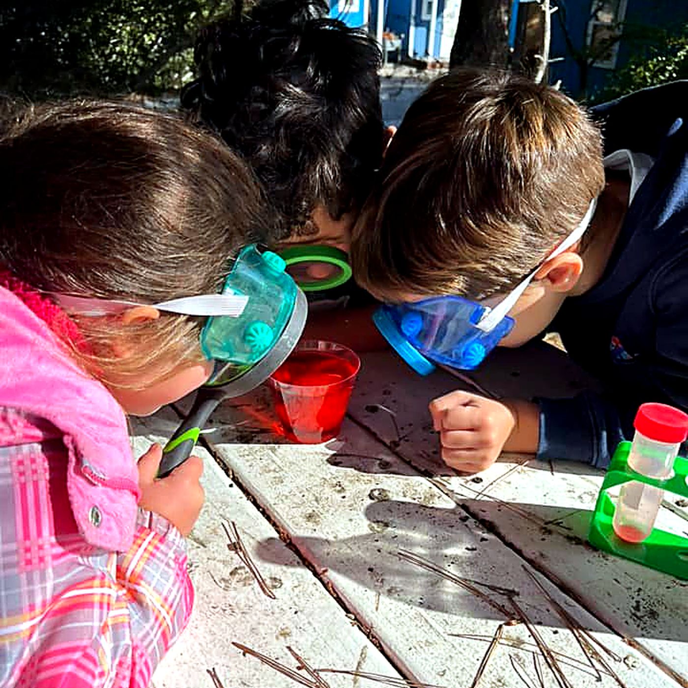 Three children in safety goggles leaning over a science experiment